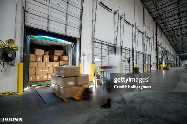 Lastkaj i en industrihall med paket och en suddig gestalt av en arbetare.